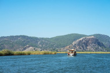 Türkiye 'nin güneybatı kıyısındaki Marmaris ve Fethiye ilçeleri arasında yer alan Mugla ilindeki Lycian mezarlarının bulunduğu kayaların yanındaki Dalyan Nehri' nde turistik gezi teknesi.