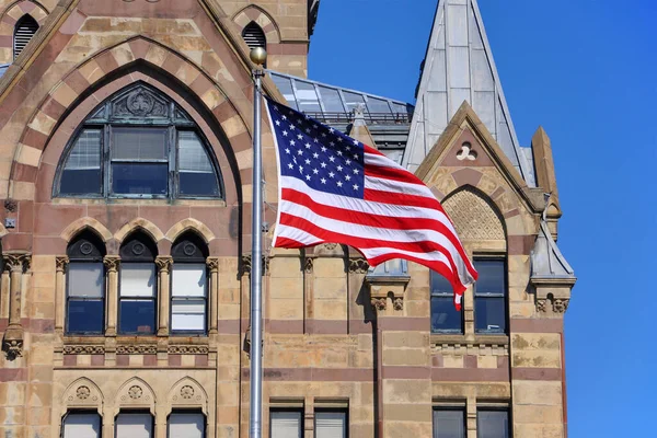 US National Flag in front of Syracuse Savings Bank Building at Clinton Square in downtown Syracuse, New York State NY, USA.
