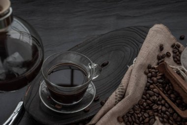 Kahve tarzı, kahve ve kahve çekirdekleri eski ahşap kepçe ve ahşap ve koyu taş arka plan etrafında kahve çekirdekleri ile roating Fincan. Metniniz için kopyalama alanı ile üstten eğik görünüm.