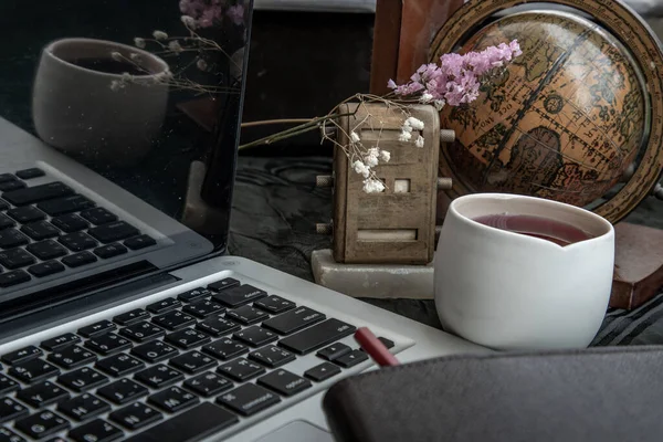 Workplace side view with laptop screen, keyboard, globe, desktop calendar, flower, fruit juice mug and notebook with pencil at office workplace. Creative concept. Blogger\'s decorated workspace. Selective focus.