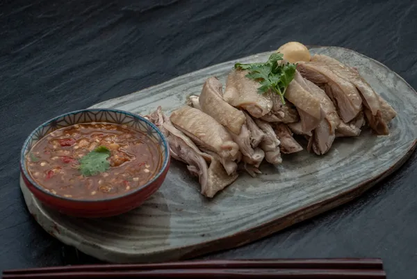 Asian food style marinated steamed chicken (Betong Chickken) and sauce on ceramic plate. Serving chilled as an appetizer. Oblique view from the top.