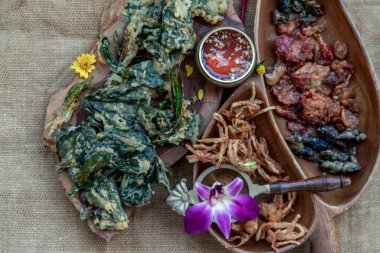 Tahta tepside tatlı sosla servis edilen gevrek çiçekler, çıtır otlar ve çıtır sebzeler..