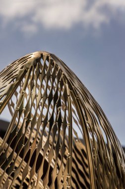 Bangkok, Tayland - 30 Haziran 2021: parkta dekoratif çekicilik için altın çelik heykel. Mimari yapı dekoratif metalden oluşur, arka planda mavi bir gökyüzüne karşı alçak bir açıdan çekilir. Seçici odak.