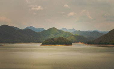 Gün doğumunda veya günbatımında arkaplanda dağlar olan göl kıyısı manzarası. Tam olarak odaklanamıyorum..
