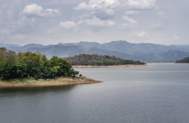 Gün doğumunda veya günbatımında arkaplanda dağlar olan göl kıyısı manzarası. Tam olarak odaklanamıyorum..