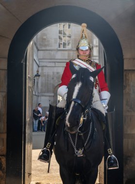 Londra, İngiltere - 19 Nisan 2019: Kraliyet kırmızı paltosu ve altın miğferiyle Kraliçe 'nin can kurtaranlarından biri Kraliyet Sarayı' nda siyah bir atın üzerinde oturuyor. Seçici odak.