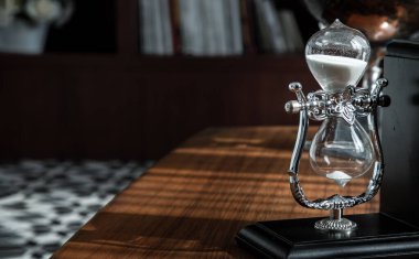 Chiang Rai,Thailand - Sep 06, 2020 : Hourglass on desk with the background of bookshelves in library. Past moments concept with copy space, Selective focus.