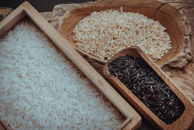 Çeşitli pirinç türleri: esmer pirinç, Yasemin pilavı, eski ahşap arka planda Riceberry. Organik çiğ pirinç koleksiyonu, sağlıklı gıda ve diyet konsepti, genel görünüm, seçici odaklanma.