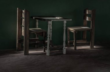 İki ahşap sandalye ve yeşil beton duvarın önünde duran eski ahşap beyaz masa. İçinden bir ışık huzmesi geçen boş bir odada. Koyu ton, metin için boşluk, Seçici odak.