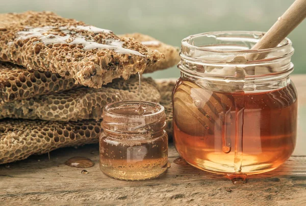 Cam kavanozdaki taze bal peteklerinden damlayan ve eski ahşap masa üzerinde tahta bal kovanı çubuğu olan lezzetli bal yakın plan. Sağlıklı organik natura, bal, metin için alan, seçici odak.
