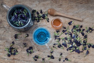 Kelebek bezelye çayı (Klitorya) veya Çaydanlıkta organik mavi anchan ve Eski ahşap arka planda bal ile servis edilen cam bardak. Sağlıklı detoks bitkisel içecek, üst görünüm, seçici odaklanma.