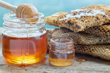 Cam kavanozdaki taze bal peteklerinden damlayan ve eski ahşap masa üzerinde tahta bal kovanı çubuğu olan lezzetli bal yakın plan. Sağlıklı organik natura, bal, metin için alan, seçici odak.