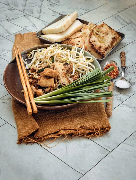 Stir fried soft turnip cake or Fried radish cake (chai tow kway) with bean sprout and chives in ceramic plate served with suger, ground dried chili. Thai - Chinese food called Kanom Pak kad or Char Koay Kak, Top view, Selective focus.