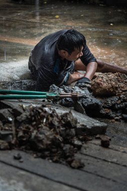 Bangkok, Tayland - 27 Haziran 2022: Yağmur sırasında ticari su kaynakları için bozuk su şebekesini tamir etmek için araç kullanan kamu işçileri. Tesisat sorunları. Odaklan ve bulanık.