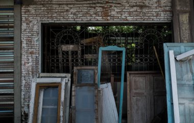 Old frames and shutters with glass from dismantled are stacked against each other front of front warehouse waiting to be sold at auction. No focus, specifically.