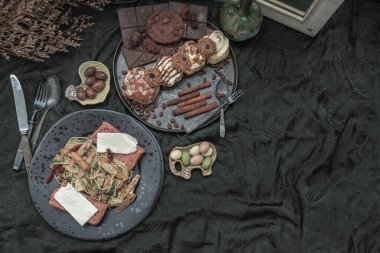 Sausage spaghetti with Cheese on bread in black ceramic plate served with Cinnamon Rolls, Dark chocolate bars, cookies and pieces in black ceramic plate on dark background. Top view, Space for text, Selective Focus.