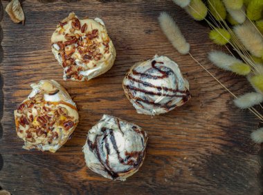 Two Cinnabon Chocobon (Soft Chocolate Buns) topped with rich cream cheese frosting and Two Caramel Pecanbon topped with decadent caramel frosting and pecans on wooden cutting board. The concept of delicious food, Top view, Selective Focus.