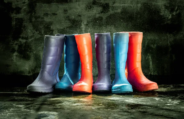 Three pairs of a colorful rain boots on wet floor with old bare cement wall background. Space for text, Selective focus.