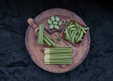 Değişik tatlara sahip yeşil atıştırmalıklar ve farklı şekillerde kavrulmuş bezelye, bisküvi kaplı Matcha kremalı bisküvi çubukları, Matcha latte krep kurabiyesi ve ahşap bir tabakaya serilmiş bademler. Yeşil Tatlılar