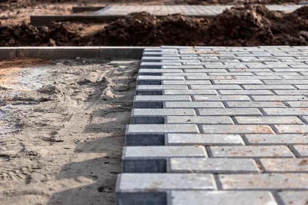 Asfalt tamiri ve kaldırım taşlarının döşenmesi, arka planda fayans küplerinin istiflenmesi. Şehrin yaya bölgesine kaldırım döşeme döşemesi, kum dolgu. Yol fayansları ve kaldırımlar