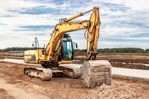 A heavy crawler excavator with a large bucket is getting ready for work in front of a panel house under construction .. Heavy construction equipment for earthworks. Quarry excavator