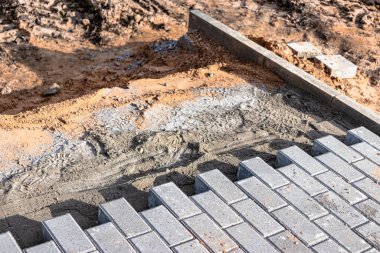 Asfalt tamiri ve kaldırım taşlarının döşenmesi, arka planda fayans küplerinin istiflenmesi. Şehrin yaya bölgesine kaldırım döşeme döşemesi, kum dolgu. Yol fayansları ve kaldırımlar