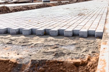 Asfalt tamiri ve kaldırım taşlarının döşenmesi, arka planda fayans küplerinin istiflenmesi. Şehrin yaya bölgesine kaldırım döşeme döşemesi, kum dolgu. Yol fayansları ve kaldırımlar