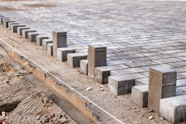 Asfalt tamiri ve kaldırım taşlarının döşenmesi, arka planda fayans küplerinin istiflenmesi. Şehrin yaya bölgesine kaldırım döşeme döşemesi, kum dolgu. Yol fayansları ve kaldırımlar