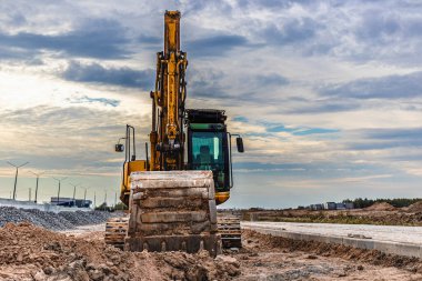 Günbatımı gökyüzünün arka planında büyük bir kova ile ağır bir sürüngen kazıcı. Toprak işçiliği için ağır inşaat malzemeleri. Bölgenin gelişimi