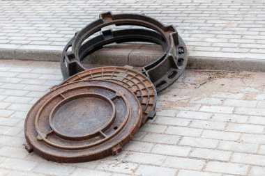 İnşaat alanında yerleştirmek için yeni dökme demir rögar kapakları hazırlanıyor. Kapaklı kapaklar kaldırım levhalarında yatıyor.