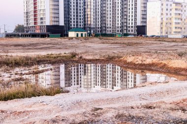 Büyük bir yerleşim yerinin şantiyesinde yağmurdan sonra büyük bir su birikintisi. İnşaat alanının sularında yansıma ve günbatımı gökyüzünün arka planında vinçler