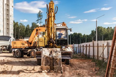 Büyük bir kova ile ağır bir sürüngen kazıcısı inşaat halindeki bir panelin önünde çalışmaya hazırlanıyor. Toprak işçiliği için ağır inşaat malzemeleri. Taş ocağı kazıcısı