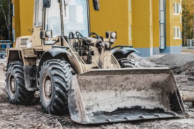 İnşaat alanında elinde kova olan ağır bir yük taşıyıcı. Toprak işçileri, taşımacılık ve malzeme yükleme ekipmanları - toprak, kum, ezilmiş taş