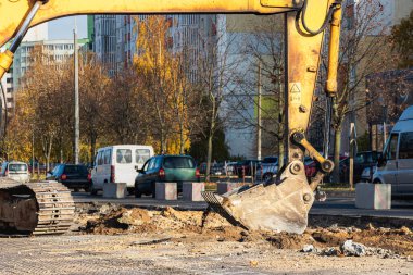 Modern bir kentte bir kazıcı yolun yeniden inşası sırasında çalışmalar yapıyor. Şehirdeki ağır inşaat malzemeleriyle tamirat yapılıyor.