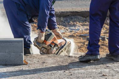 Bir inşaat işçisi gaz testeresiyle yol kaldırımını kesiyor. Yol yüzeyi tamiri. Bir kaldırım taşı kurulumu