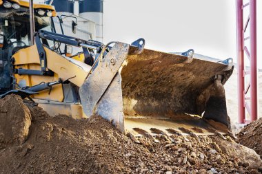 Ön kovadaki bir kazıcı inşaat alanındaki toprağı temizliyor. Toprak işçiliği için inşaat malzemeleri. Yakın plan.