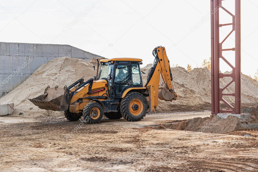 An excavator in the front bucket removes soil for backfill at the construction site. Construction equipment for earthworks