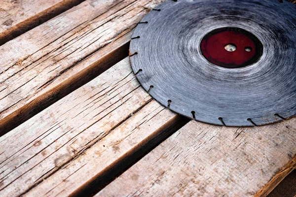 A circular saw blade rests on a wooden plank surface. Old diamond blade for cutting concrete and stone. Soft selective focus