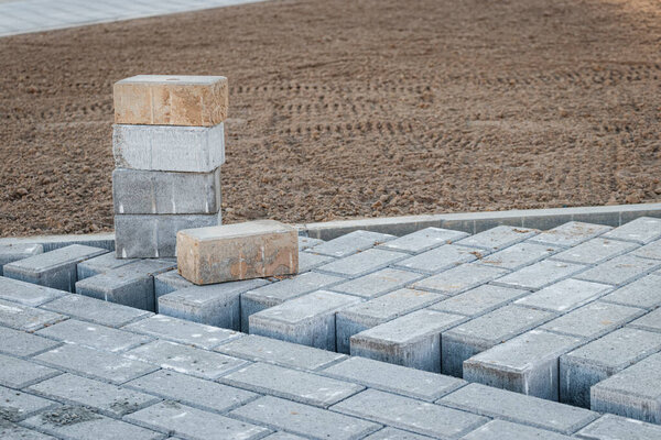 Ремонт тротуаров и укладка тротуарных плит на дорожке, укладка плиточных кубиков на заднем плане. Укладка тротуарных плит в пешеходной зоне города, заполнение песком. Дорожная плитка и бордюры