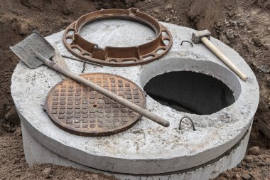 İnşaat alanına su ve kanalizasyon için güçlendirilmiş beton kuyusu kurulması. Demir kapaklı ve inşaat aletli halkalar.