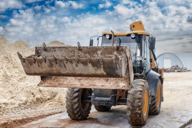 Kazı makinesi ön kovayla çukuru dolduruyor. İnşaat alanında toprağı hareket ettiriyor. Yakın plan. Ağır inşaat ekipmanları