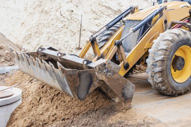 Kazı makinesi ön kovayla çukuru dolduruyor. İnşaat alanında toprağı hareket ettiriyor. Yakın plan. Ağır inşaat ekipmanları
