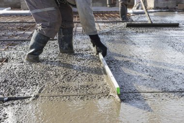 İşçi inşaat alanına zemini dökerken esasen betonu düzleştirir.