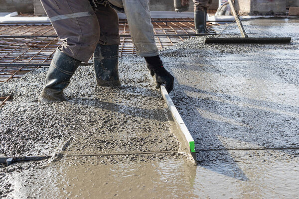 The worker levels the concrete by rule when pouring the floor on the construction site