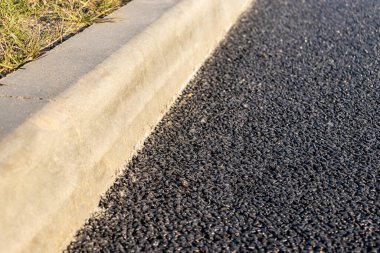 Yolda beton kaldırım boyunca yeni asfalt döşenmiştir. Yakın plan. Yol onarımı