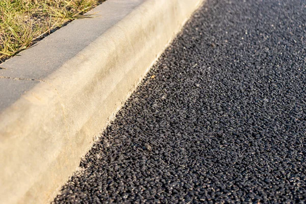 Yolda beton kaldırım boyunca yeni asfalt döşenmiştir. Yakın plan. Yol onarımı