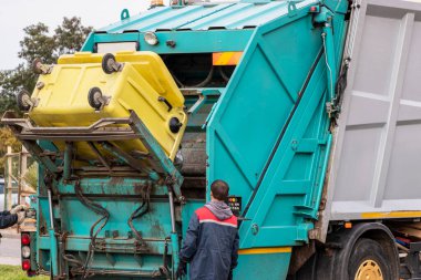 Bir çöp kamyonu yerleşim alanından çöp topluyor. İşçiler bir konteynırı çöplerle doldurur. Toplama ve çöpleri ayır