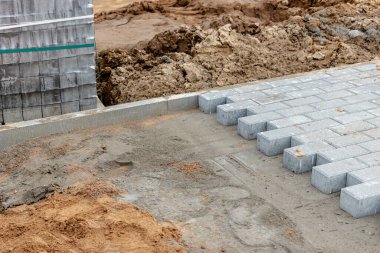Asfalt tamiri ve kaldırım taşlarının döşenmesi, arka planda fayans küplerinin istiflenmesi. Şehrin yaya bölgesine kaldırım döşeme döşemesi, kum dolgu. Yol fayansları ve kaldırımlar