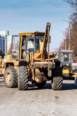 Ağır bir yükleyici toprağı kovayla taşır ve yolu derecelendirir. Sonbaharda modern bir şehrin merkezinde yol onarımı. Toprak taşımak için ağır inşaat makineleri