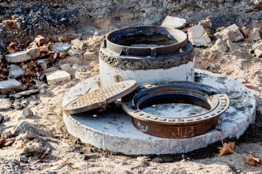 İnşaat alanına yerleştirmek için yeni dökme demir kapaklar hazırlanıyor. Kapaklı kapaklar, düşmüş sonbahar yapraklarının arka planında yerde yatar.